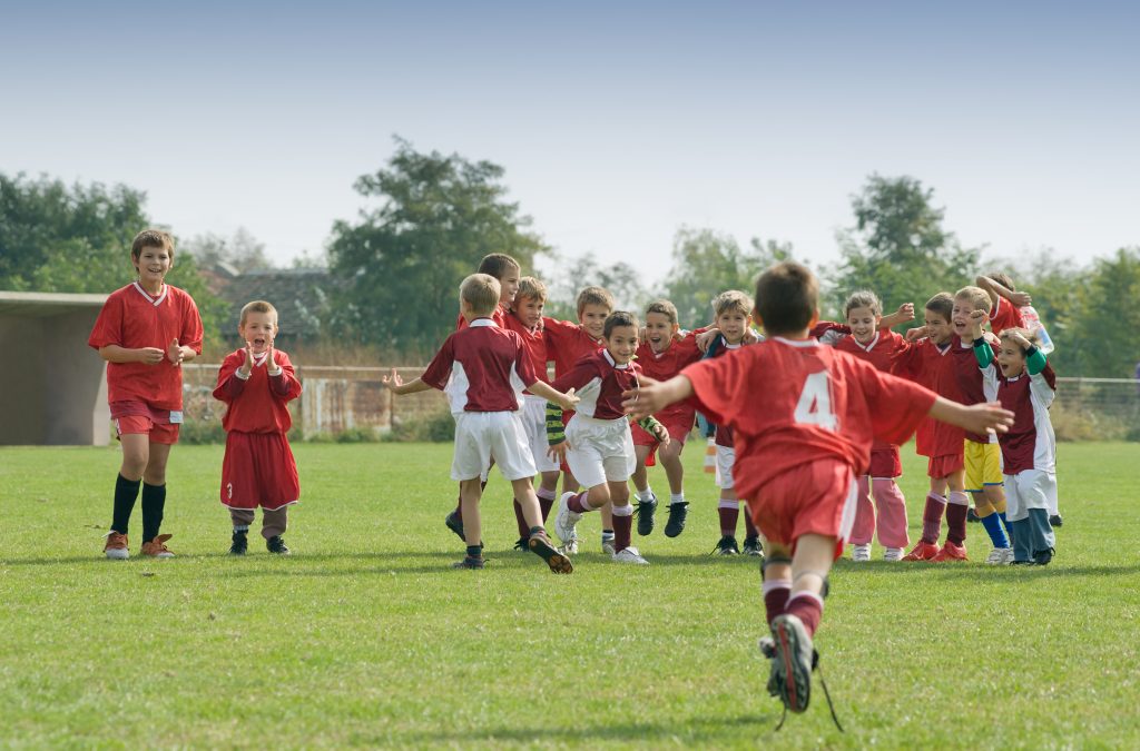 Football kid player running to his teammates, on the field